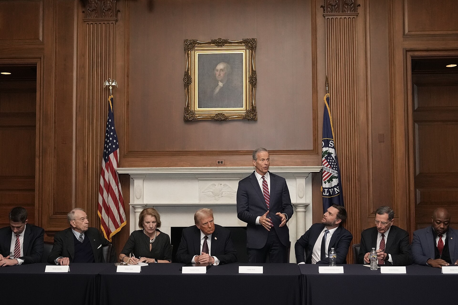 Senate Majority Leader John Thune stands to speak at a table with President Trump, Vice President JD Vance and Republican senators