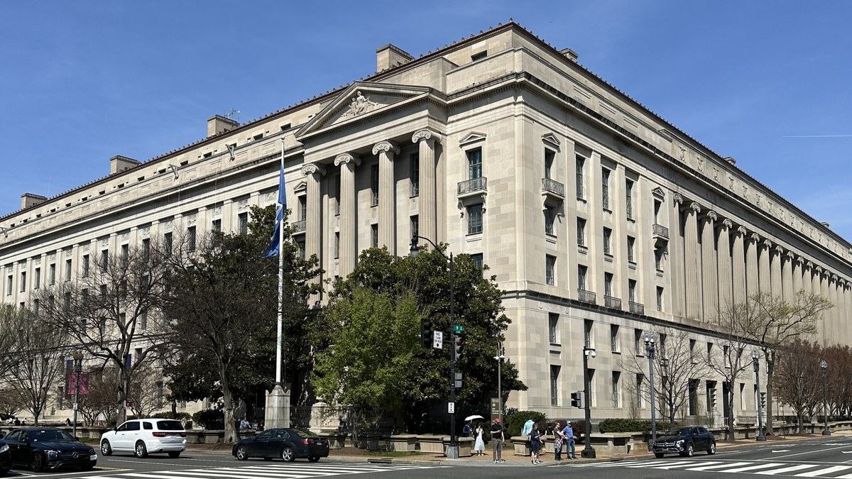 The Robert F. Kennedy Department of Justice Building in Washington, D.C., a limestone neoclassical building with columns, seen from a street corner under blue sky.