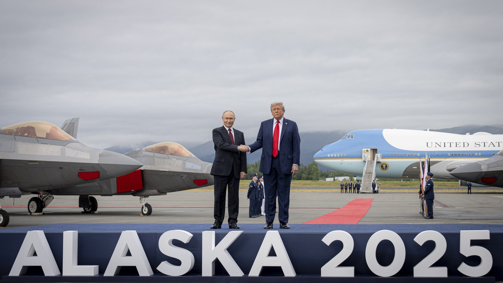 President Donald Trump and Russian President Vladimir Putin shake hands on a stage reading "Alaska 2025" at Joint Base Elmendorf-Richardson, with F-22 jets and Air Force One behind them.