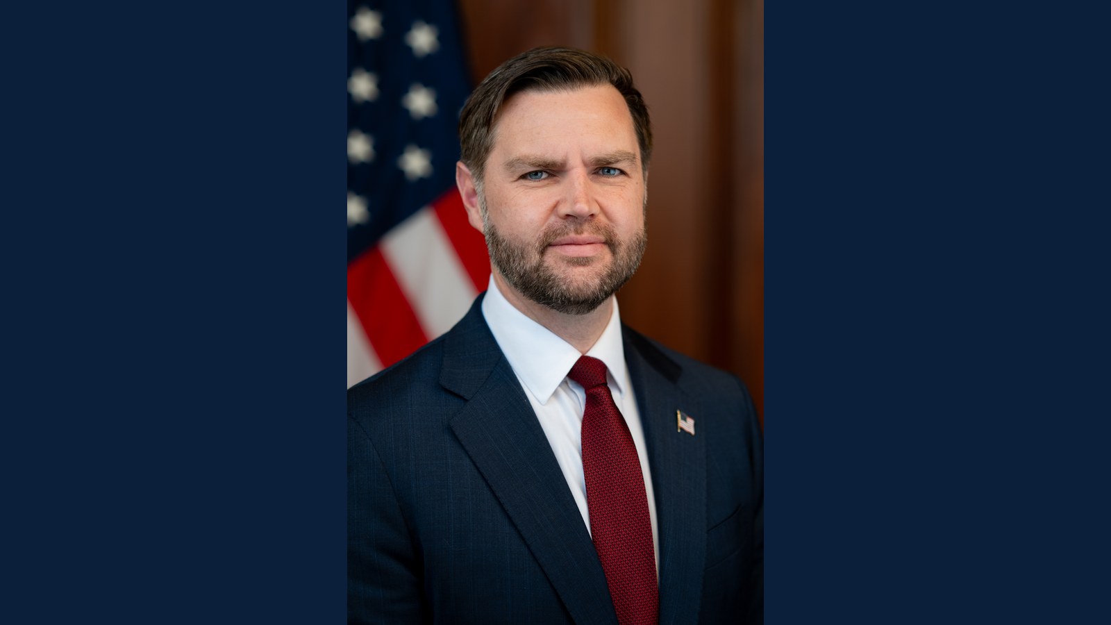 Official portrait of Vice President JD Vance in a navy suit and red tie in front of an American flag.