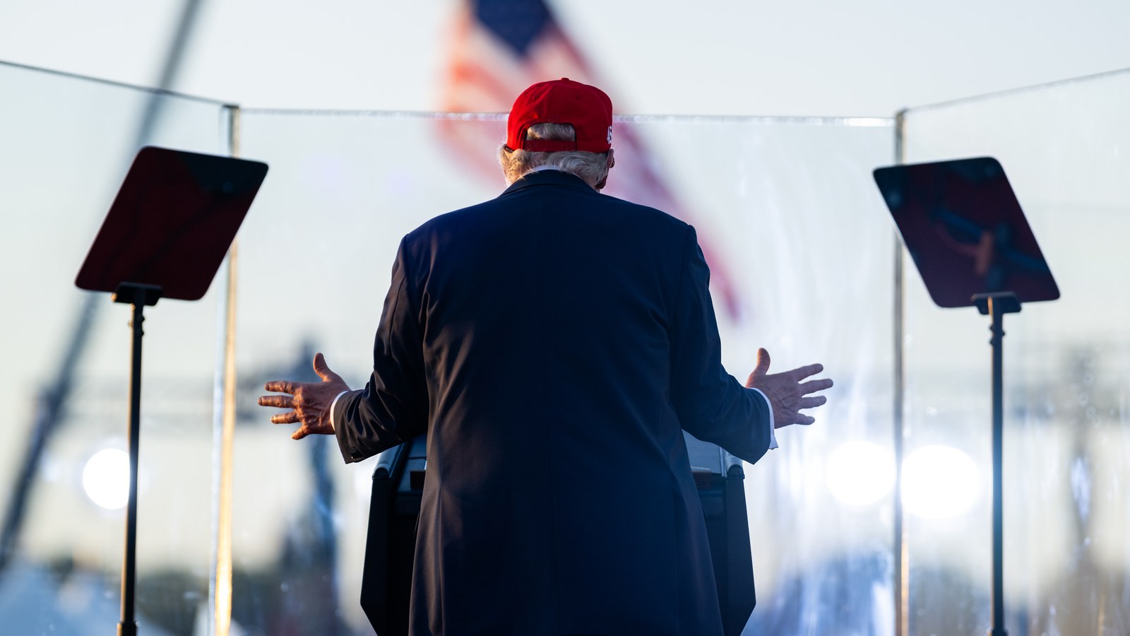 President Donald Trump, seen from behind, speaks at an outdoor rally podium in Des Moines, Iowa, in July 2025