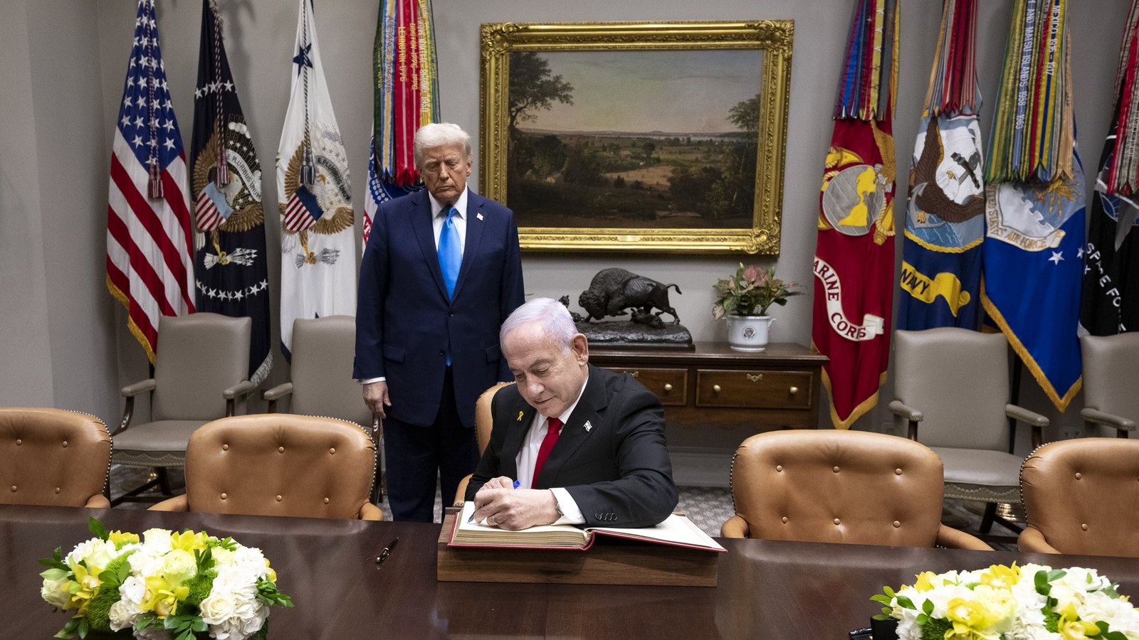 Israeli Prime Minister Benjamin Netanyahu signs a guest book as President Donald Trump stands behind him at the White House