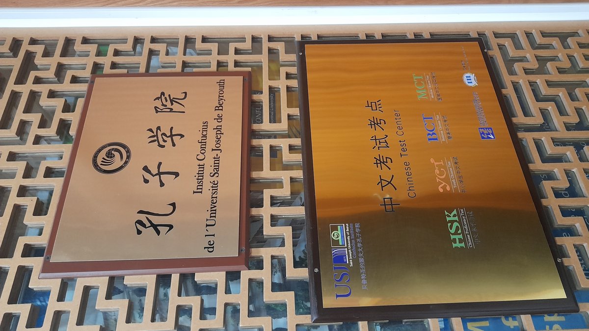 Confucius Institute name plaque in Chinese and French beside a Chinese test center sign on a university campus